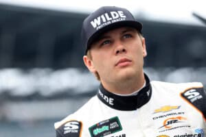 Young NASCAR driver in racing suit looking focused at the race track.